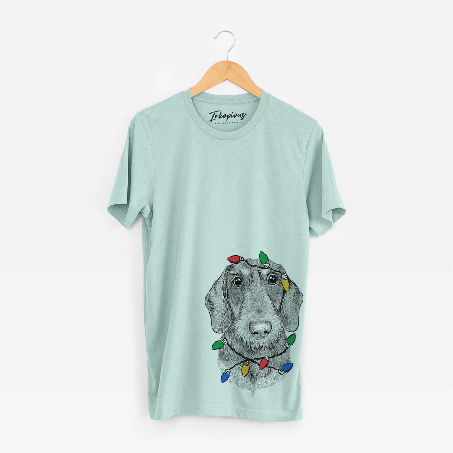 Hand-drawn sketch of Truman the Wirehaired Dachshund wrapped in Christmas lights on a Heather Sage Unisex crewneck